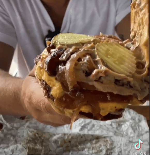 Screenshot of man holding up an opened cheeseburger