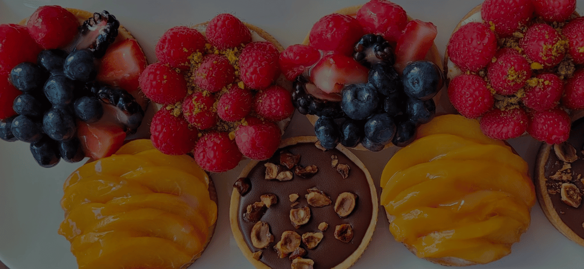 Assorted mini fruit tarts topped with raspberries, blueberries, strawberries, mango slices, and chocolate hazelnut glaze