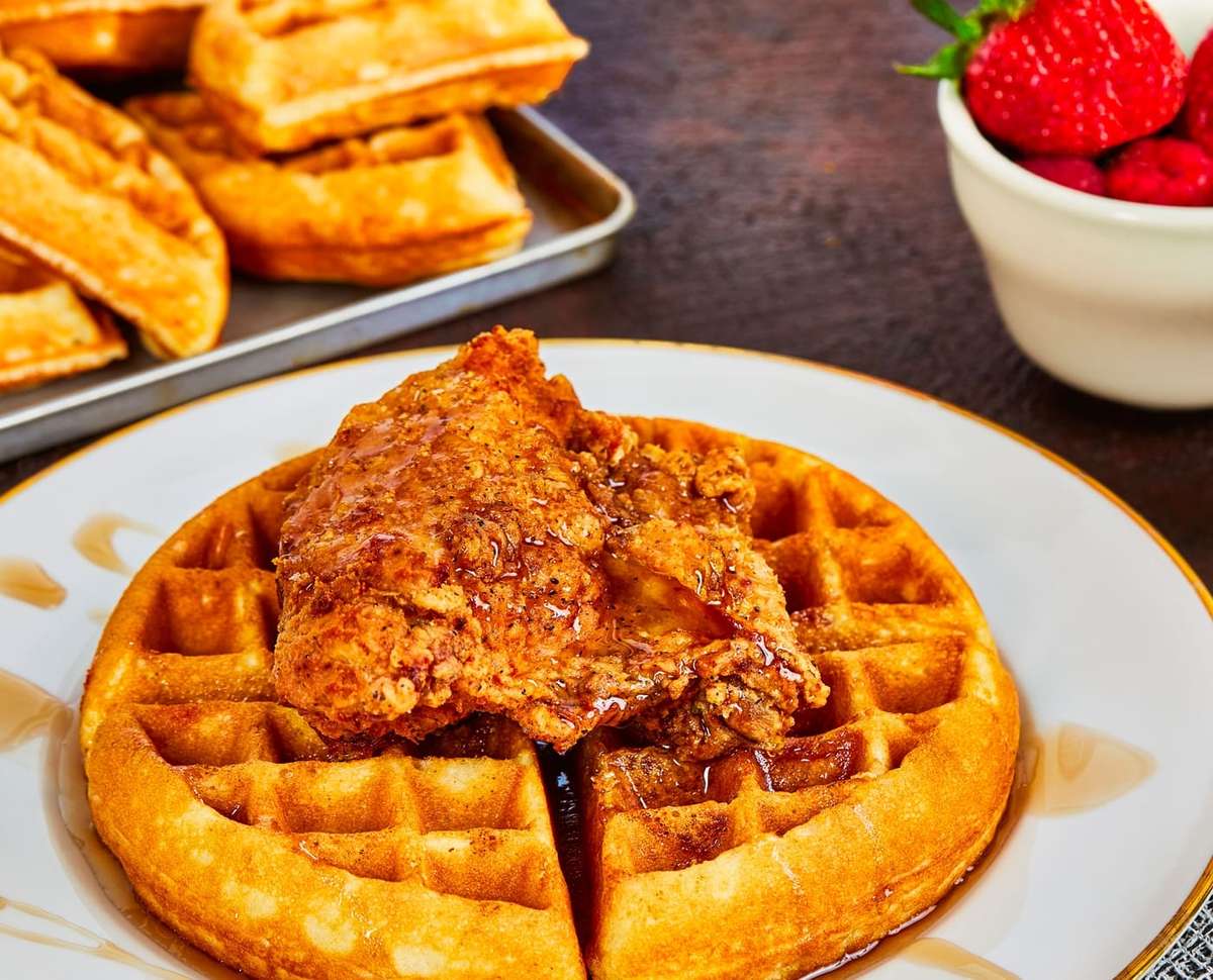 Fried chicken and waffles topped with syrup, served with fresh strawberries and additional waffles on the side.