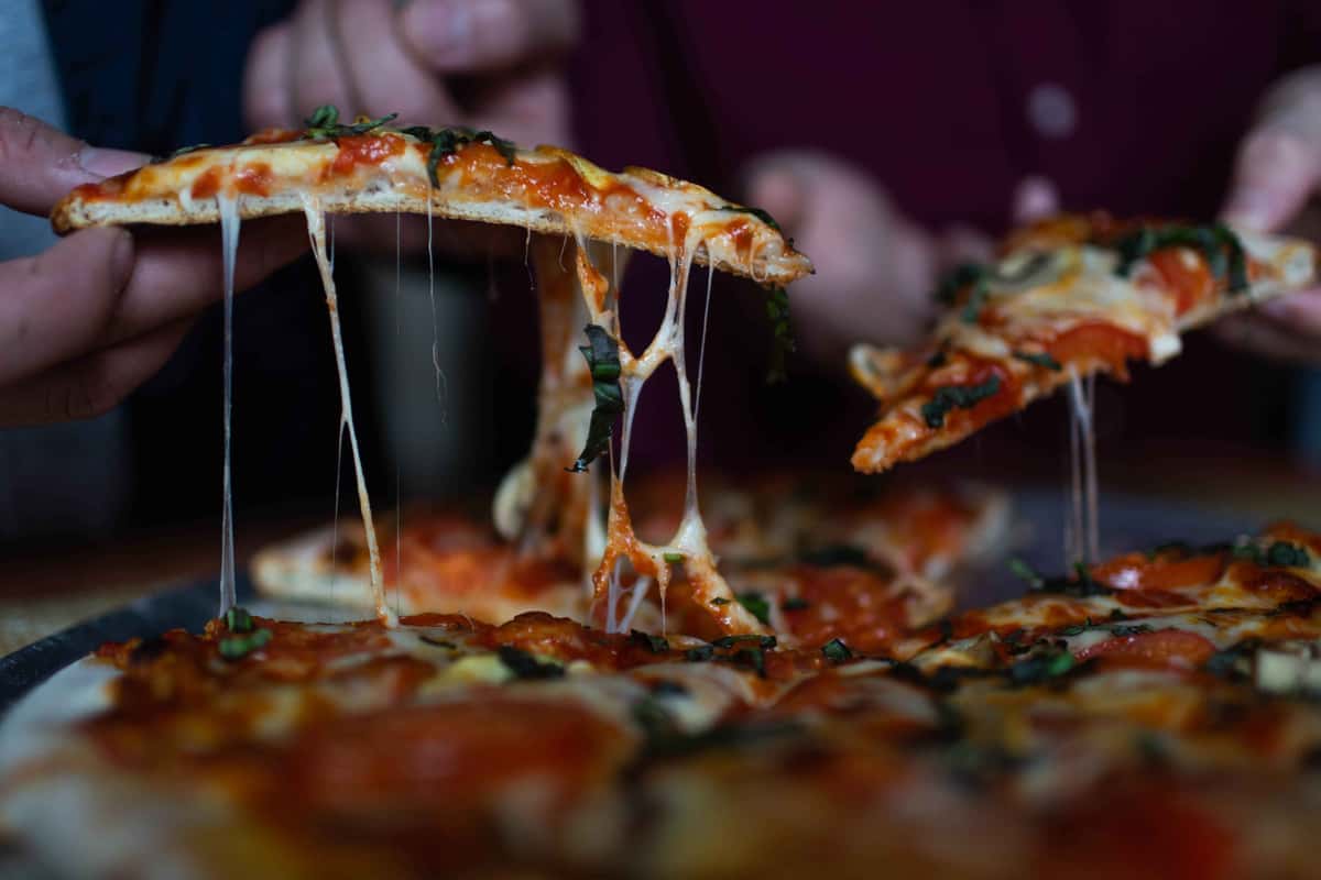 Two people lifting pizza slices, with long strands of melted cheese stretching from the pie.