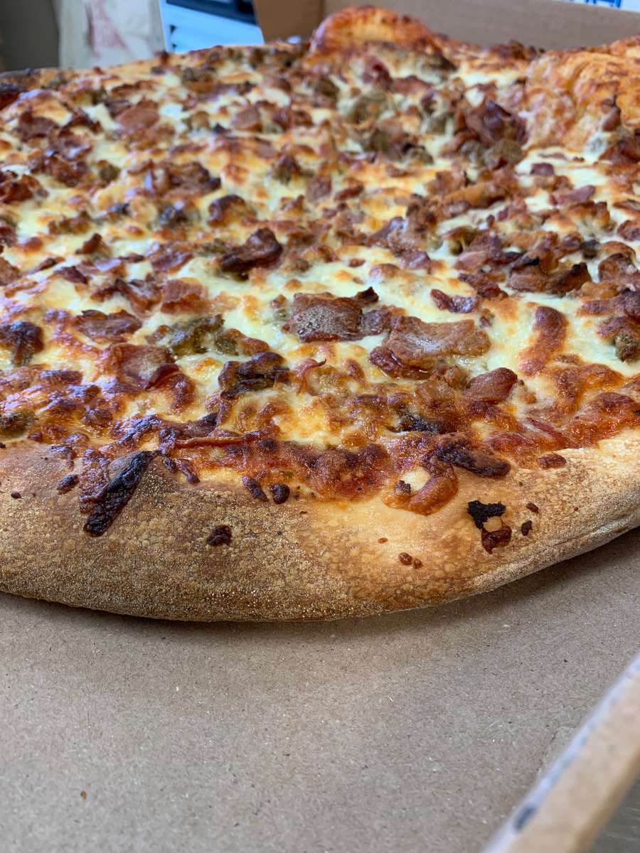 Close-up of a meat-topped pizza with melted, browned cheese and a thick golden crust inside a cardboard box.