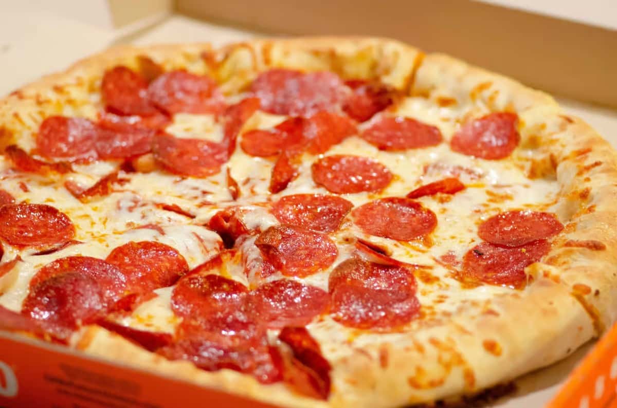 Close-up of a pepperoni pizza with melted cheese and a thick golden crust inside a box.