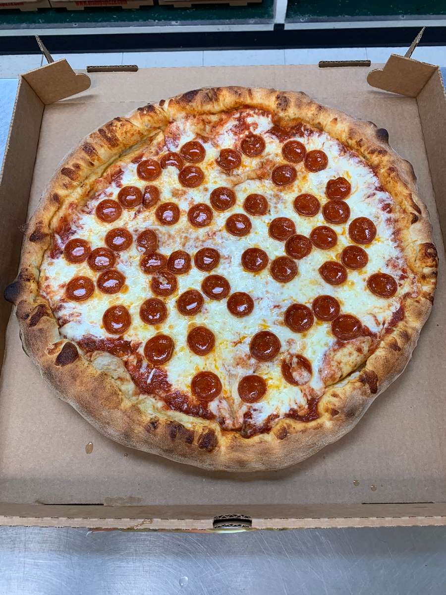 Large pepperoni pizza with melted mozzarella and a charred, golden crust in an open cardboard box.