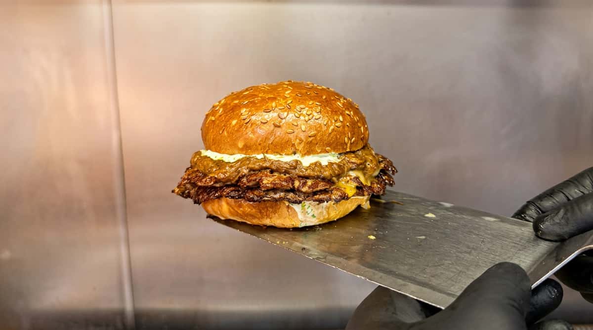 Double smashburger with cheese, sauce, and a sesame seed bun on a metal spatula.