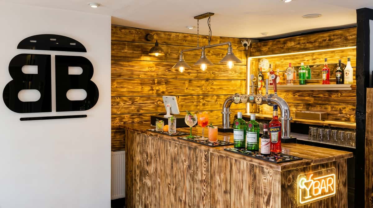 A modern bar interior with a distressed wood counter and back wall, beer taps, liquor bottles on shelves, and a neon "Bar" sign.