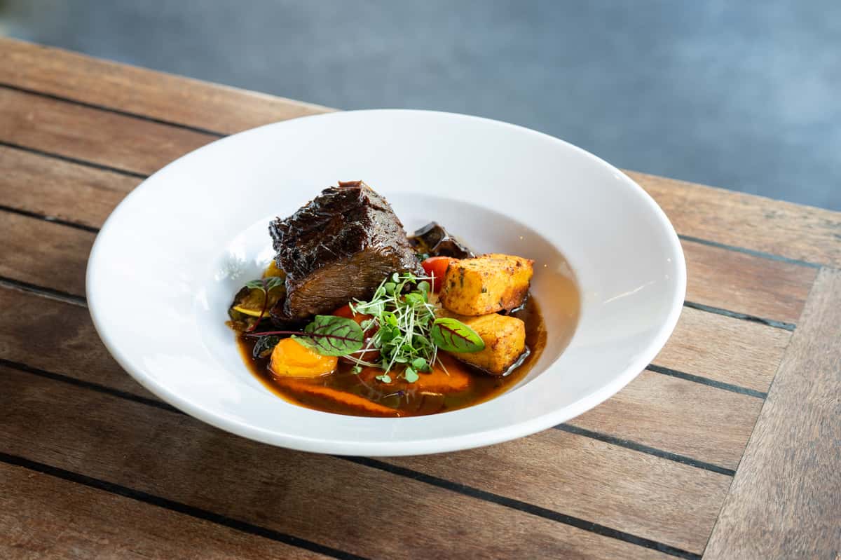 Braised beef served with roasted potatoes, vegetables, sauce, and fresh herbs.