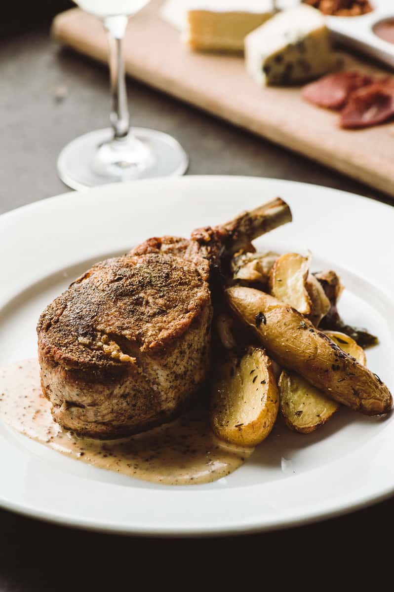 Grilled bone-in pork chop served with roasted potatoes and a creamy sauce.