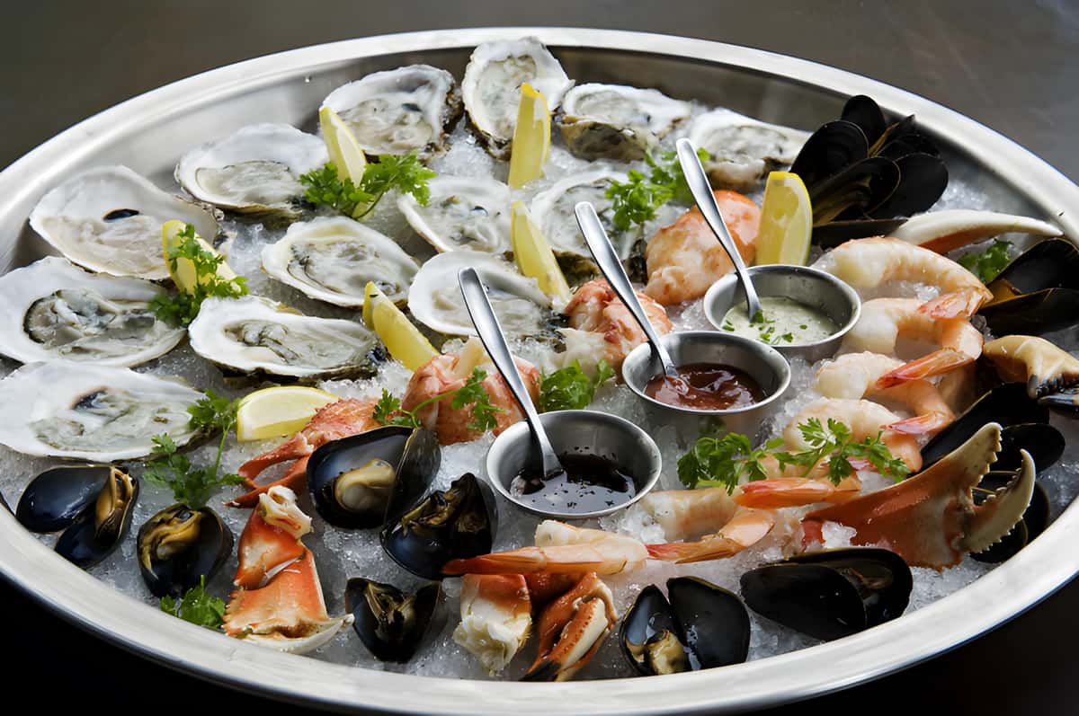 Large seafood platter filled with oysters, shrimp, mussels, lemon wedges, and dipping sauces.