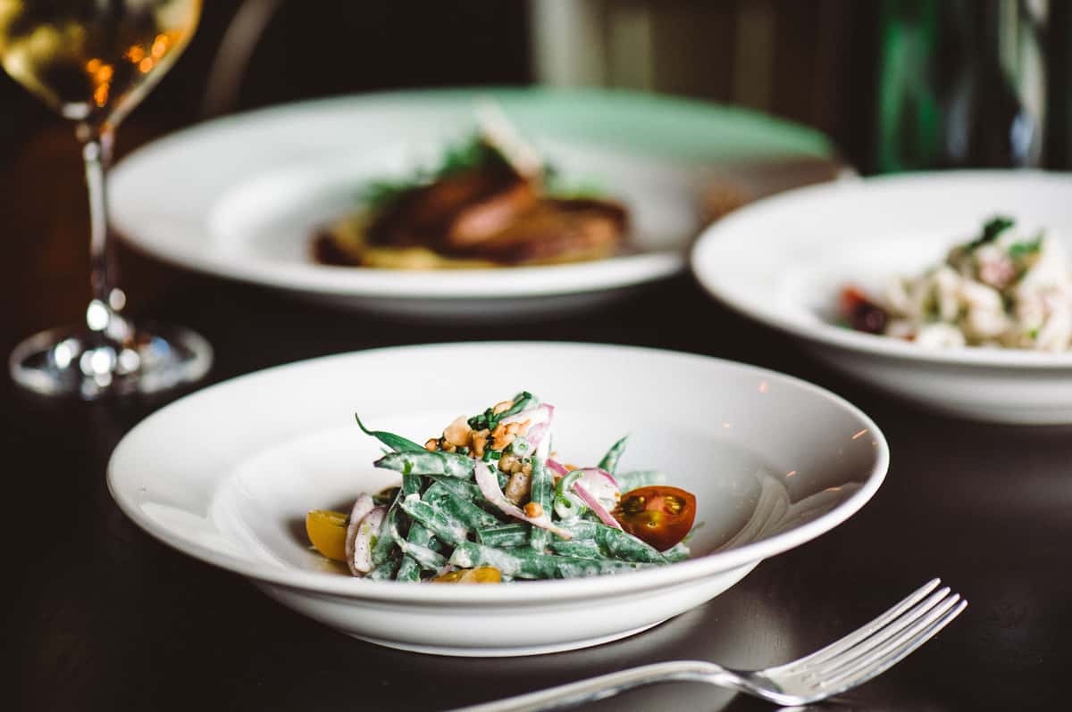 Haricot verts salad with tomatoes and herbs served on a white plate in a softly lit dining room.