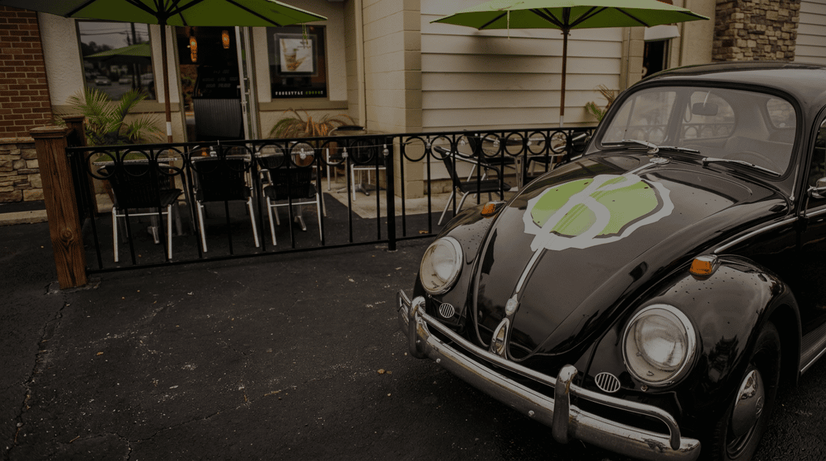 Vintage black Volkswagen Beetle parked outside Burrito Famous with branded hood artwork, next to the restaurant's outdoor patio featuring umbrella-covered seating and a casual, beach-inspired atmosphere.