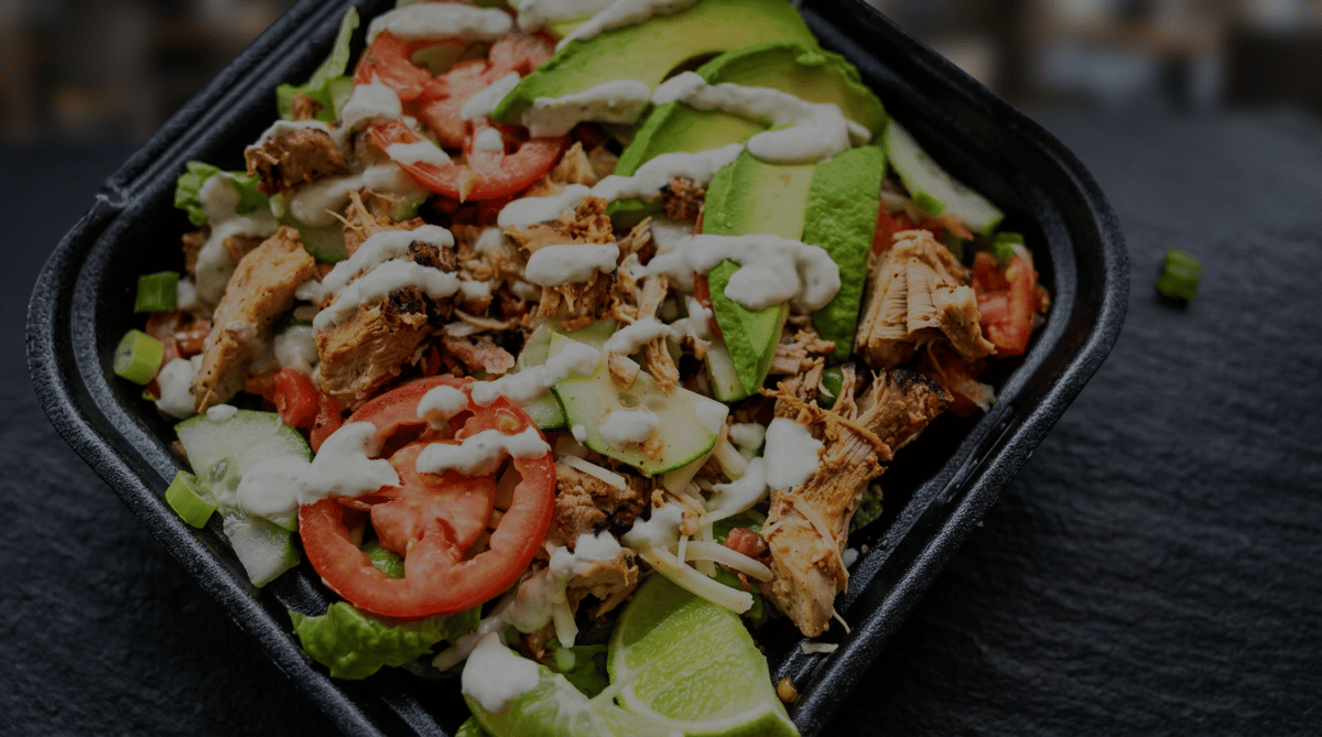 Fresh Burrito Famous salad topped with grilled chicken, sliced avocado, tomatoes, cucumbers, shredded cheese, green onions, and creamy house dressing for a healthy Mexican-inspired meal.