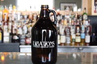 A glass Jug Growler that says “Libations a Modern American Tavern”