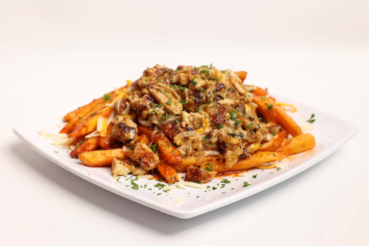 Fries, cheese, and savory toppings cover a white square plate. The dish is displayed on a clean background as part of a website gallery.