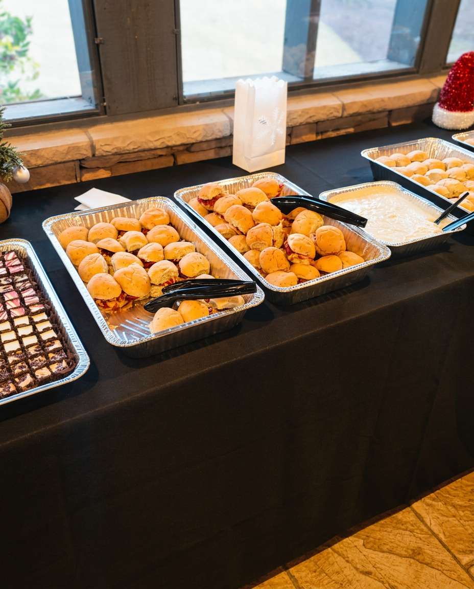 Catering from Travinia Italian Kitchen featuring trays of mini sandwiches, dipping sauce, rolls, and assorted brownies.