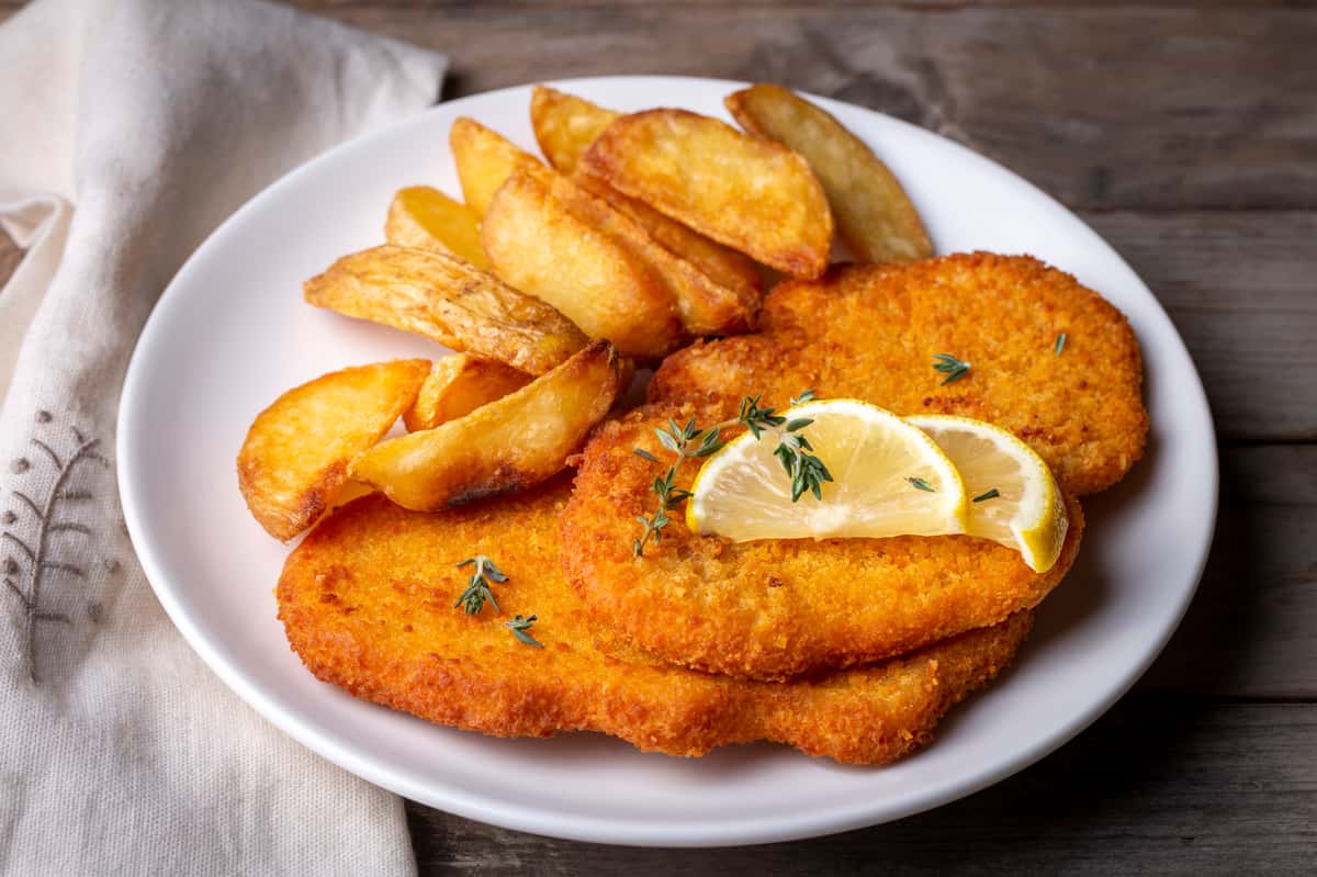 Breaded chicken schnitzel served with potato wedges and lemon slices