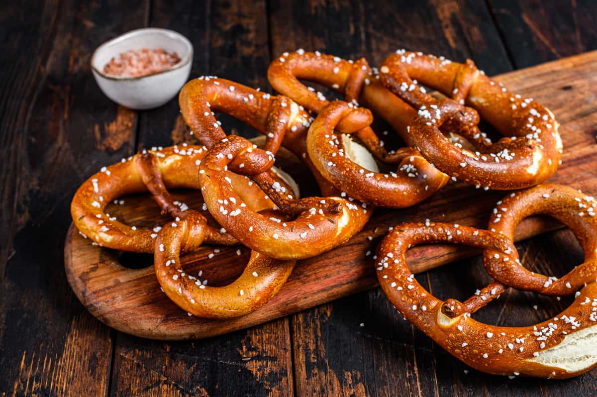 Soft baked pretzels sprinkled with coarse salt served on a wooden board with dipping sauce