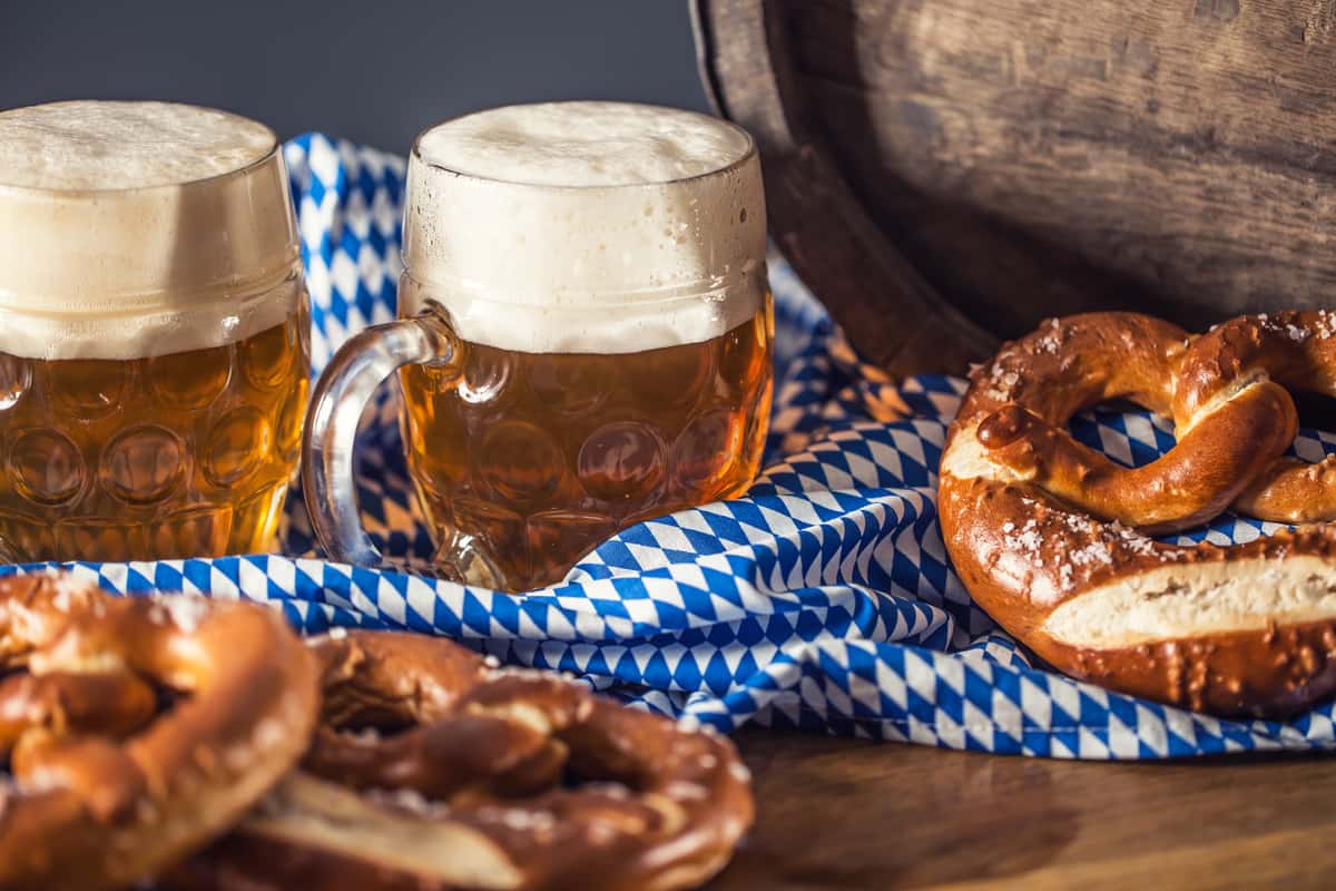 Two beer mugs filled with golden beer next to pretzels on a blue and white cloth