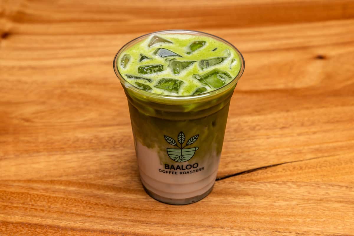 Refreshing iced matcha latte served in a clear takeaway cup, featuring vibrant green matcha, creamy milk, and ice cubes on a wooden café table.