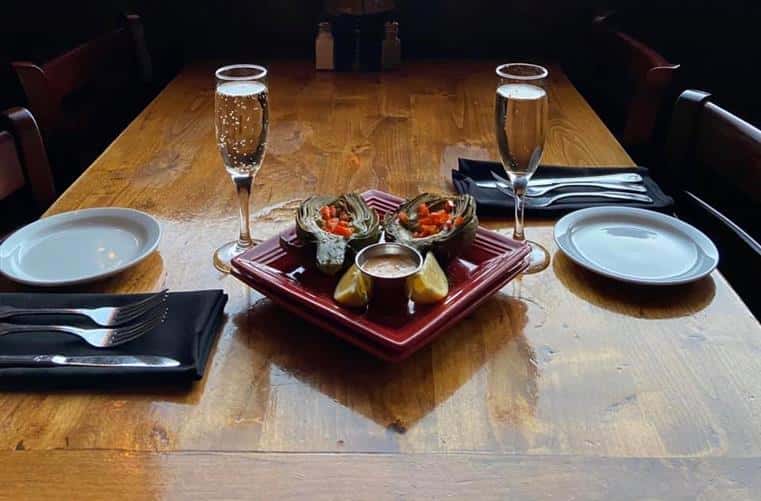 champagne and stuffed artichokes on a table with plates and utensils