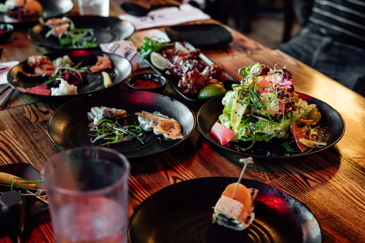Assorted gourmet dishes on a wooden restaurant table, including salad, appetizers, and sauces