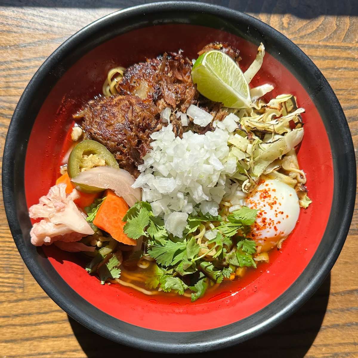 Ramen bowl with shredded meat, soft-boiled egg, pickled vegetables, onions, and lime