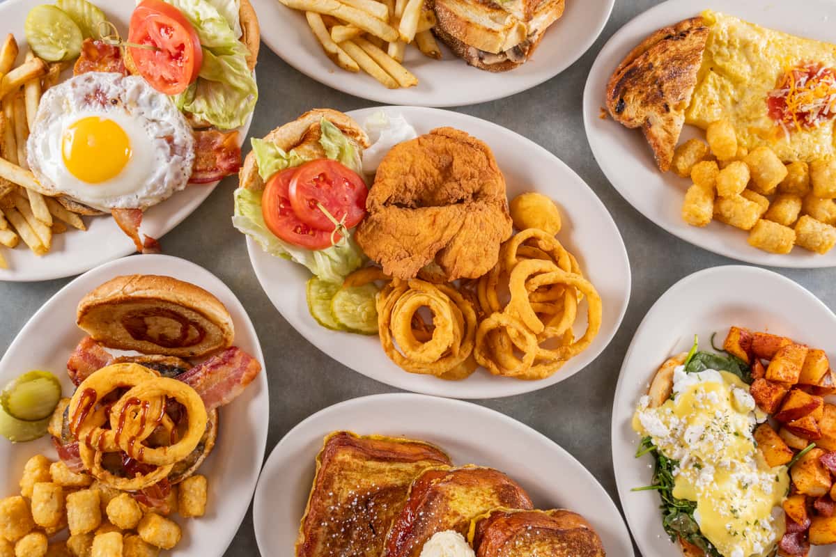Assorted breakfast and lunch plates featuring burgers, fried chicken, eggs, French toast, onion rings, and tater tots.