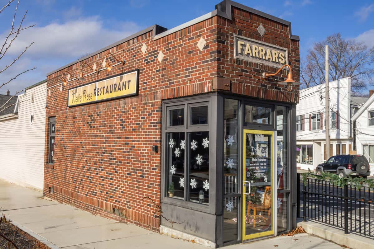 Brick building exterior of Nellie Rose Restaurant with a vintage Farrar's sign, large windows, and festive snowflake decals.