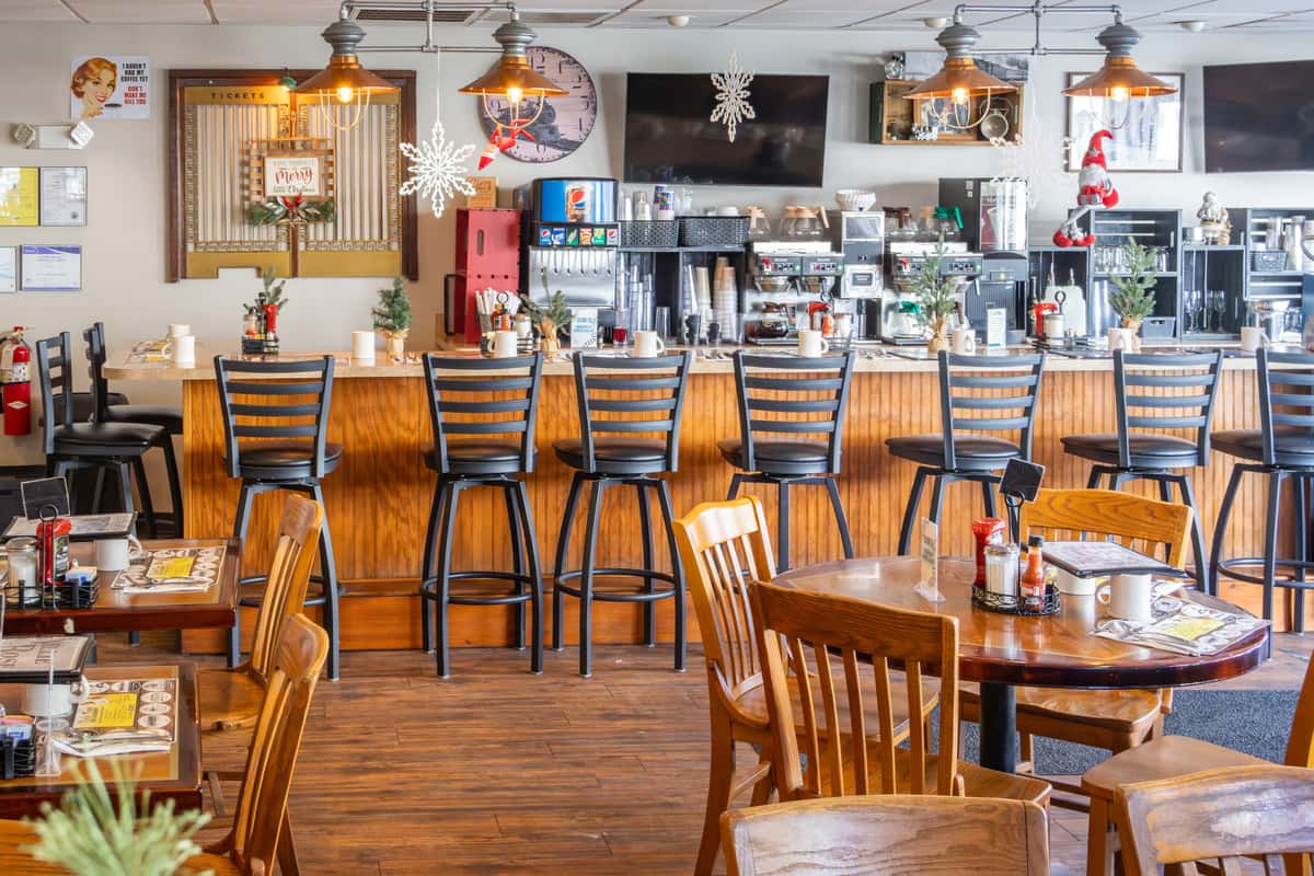 Warm and inviting diner interior with wood furnishings, counter seating, and festive holiday decorations throughout the space.