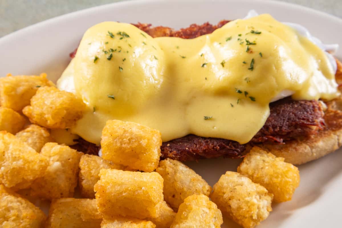 Eggs Benedict with poached eggs, hollandaise sauce, and corned beef hash on an English muffin, served with tater tots.