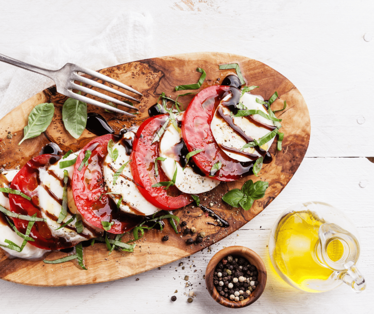 Caprese salad with sliced tomatoes, fresh mozzarella, basil, and balsamic glaze on a wooden board.