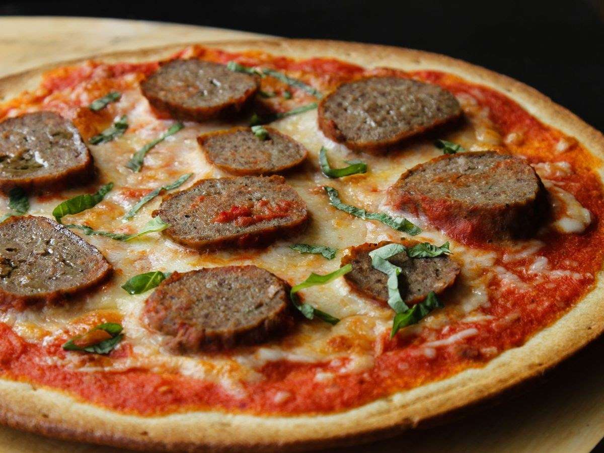 thin crust pizza with cheese, basil and sausage on top