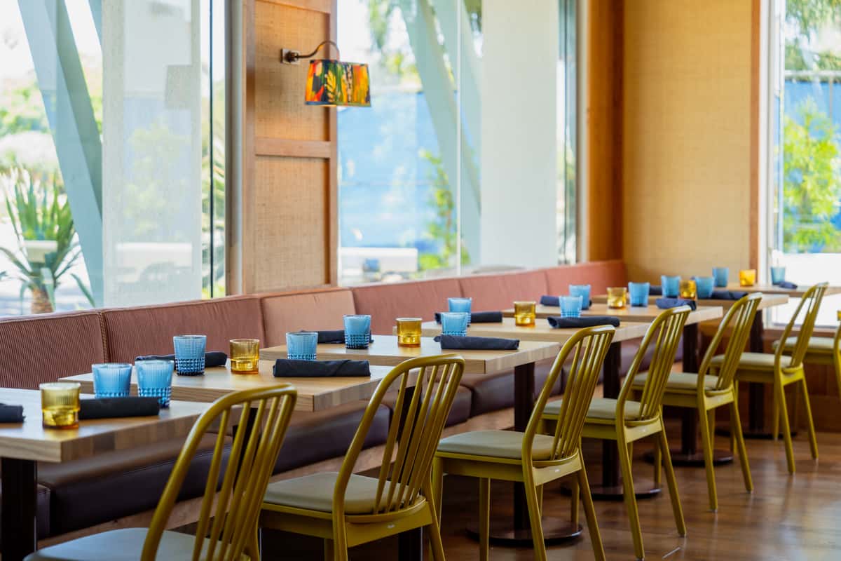 An inviting dining area featuring wooden furniture, large windows, and decorative plants.
