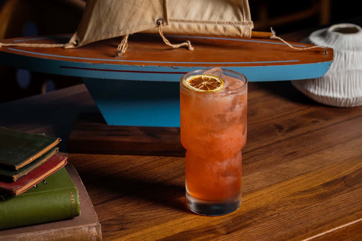 Brush with the Devil cocktail with dried citrus garnish sits on a wooden table.