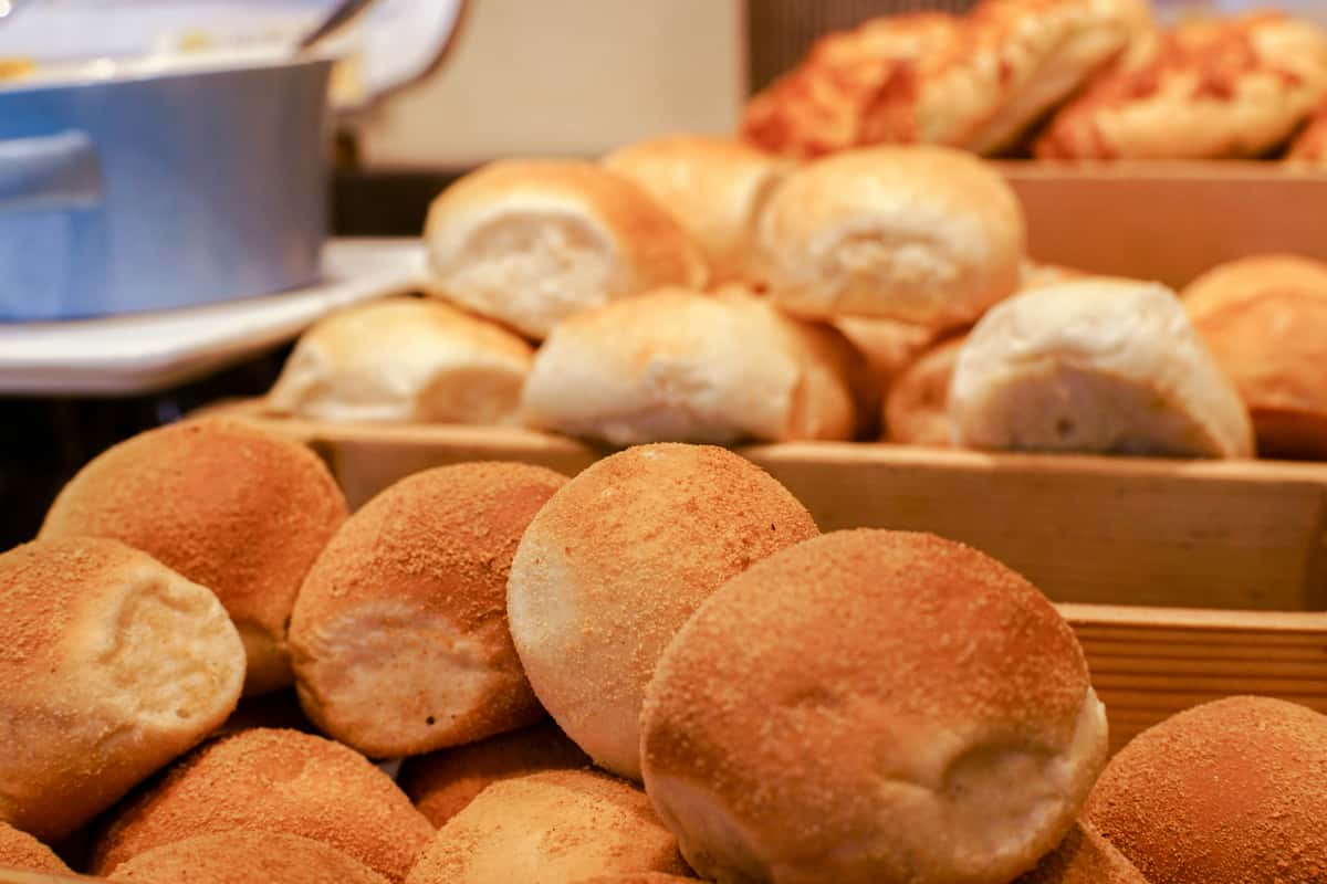 Stacks of freshly baked bread rolls displayed in wooden trays at a bakery or buffet.