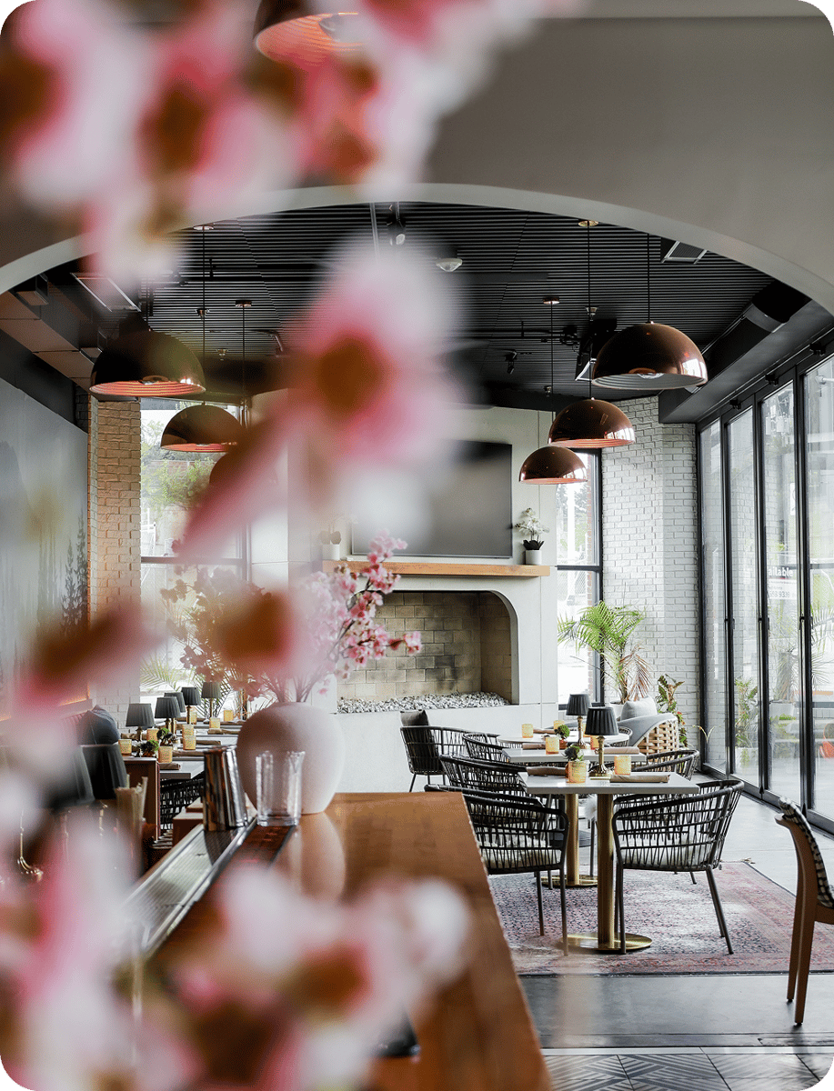 A stylish restaurant interior featuring modern seating, copper pendant lights, and a fireplace. Floral arrangements add a touch of elegance to the space.