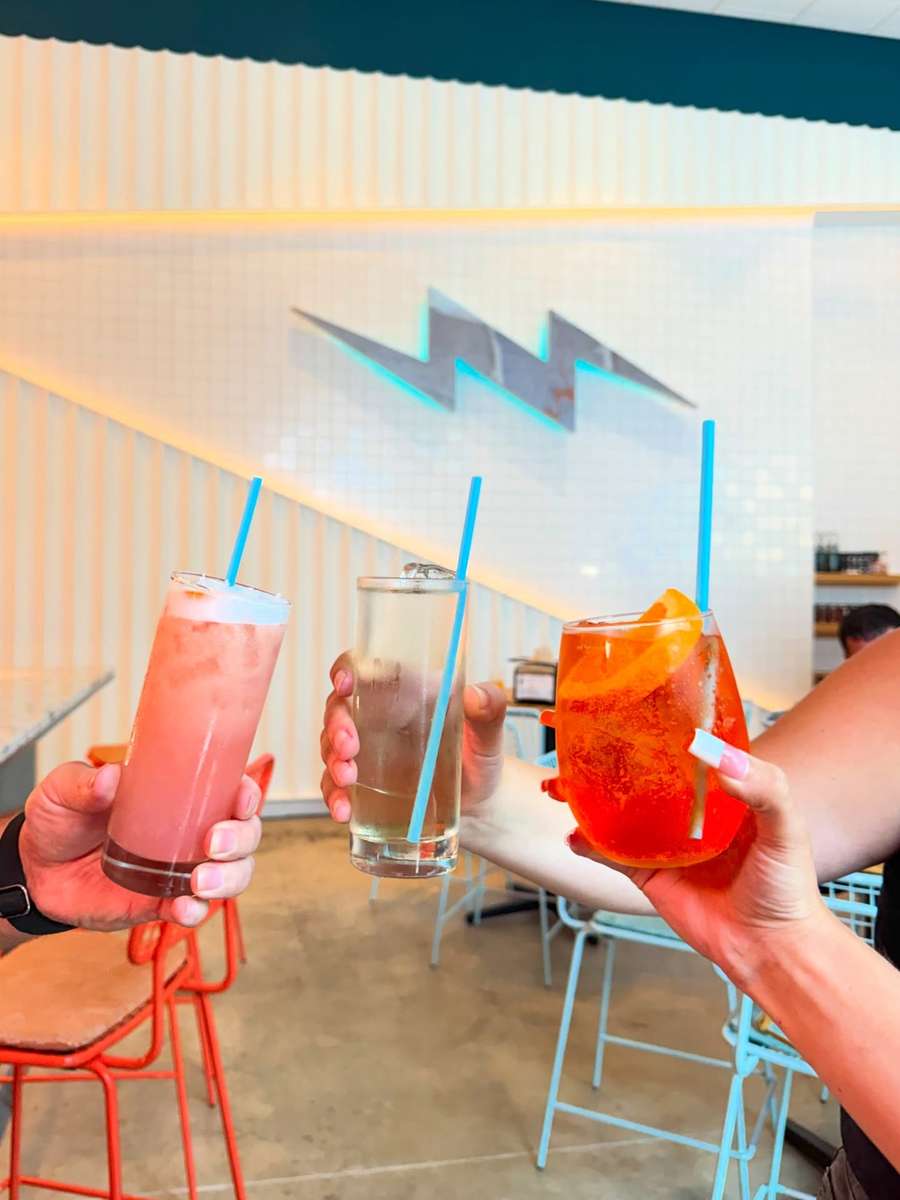 Two guests toasting drinks under the bulb-lit arch during happy hour.