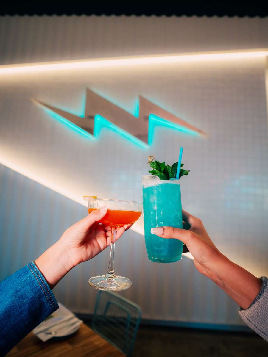 Two guests clinking cocktails in front of the teal lightning bolt wall.