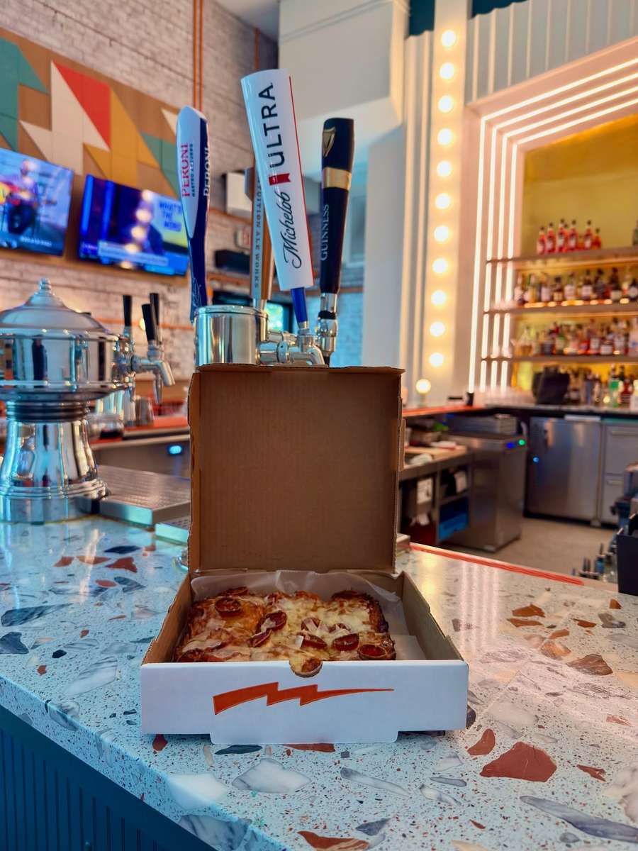 A boxed Electric Dough Pizza Co. pan pizza ready to go on the terrazzo counter.