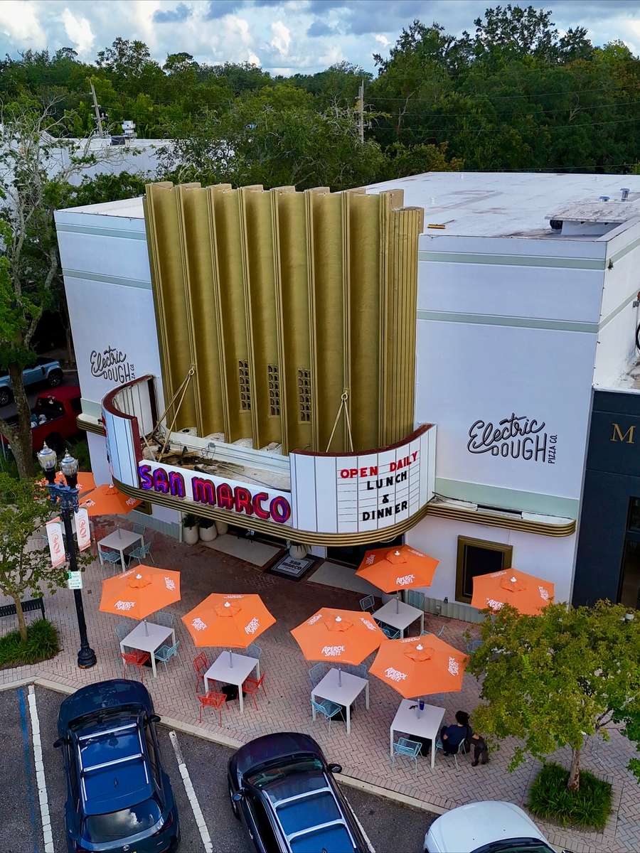 The San Marco Theatre in Jacksonville from above, its Art Deco fluted tower and lit marquee over the patio tables at Electric Dough Pizza Co.