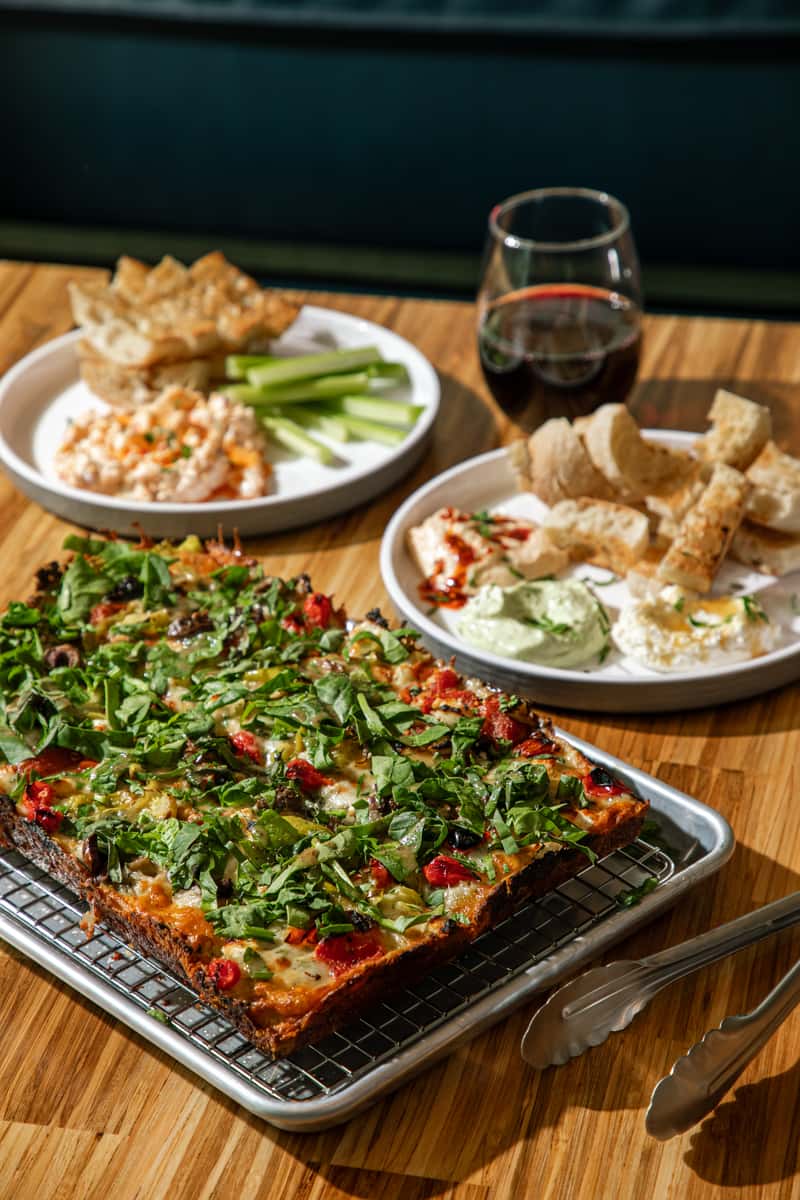 A garden pan pizza with a blackened, caramelized crust edge, served with dips.