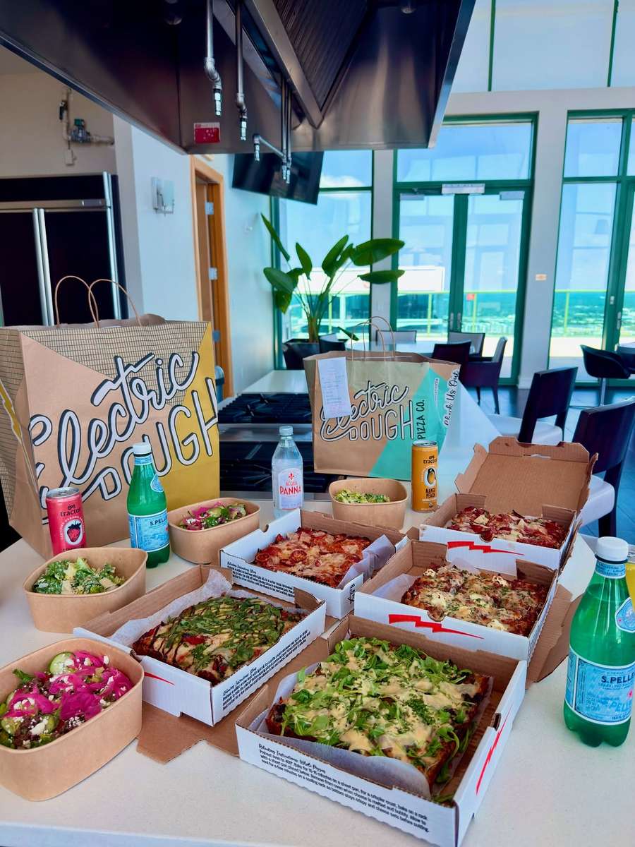 Electric Dough Pizza Co. catering boxes of pizza and salads laid out for a group.