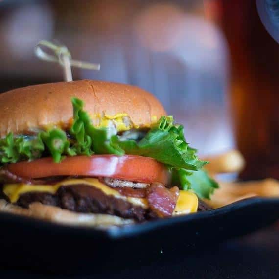 bacon cheeseburger with lettuce, tomatoes, and mustard with a toothpick