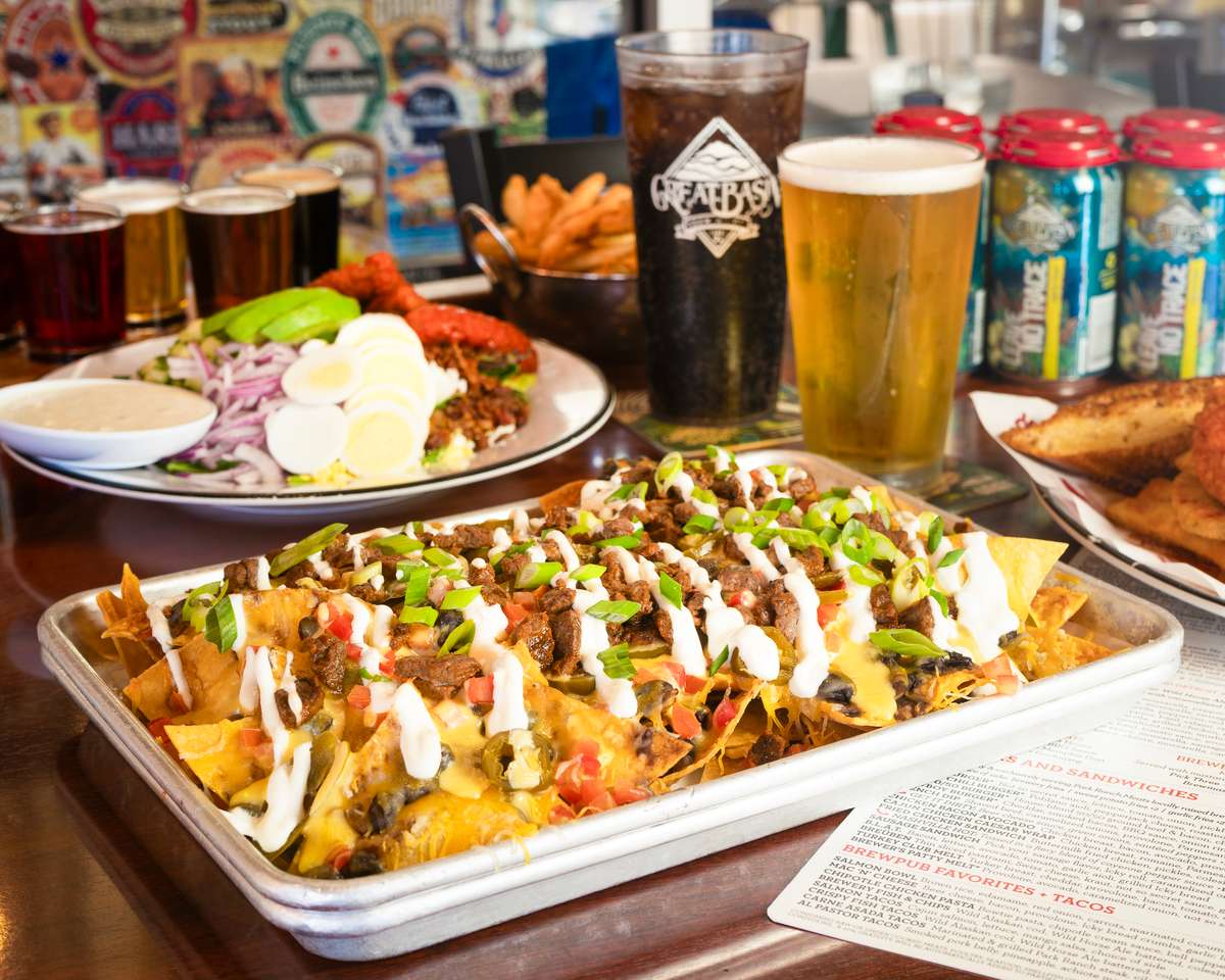 large steak nachos with avocado next to a buffalo cobb, a coke, and pint of beer.