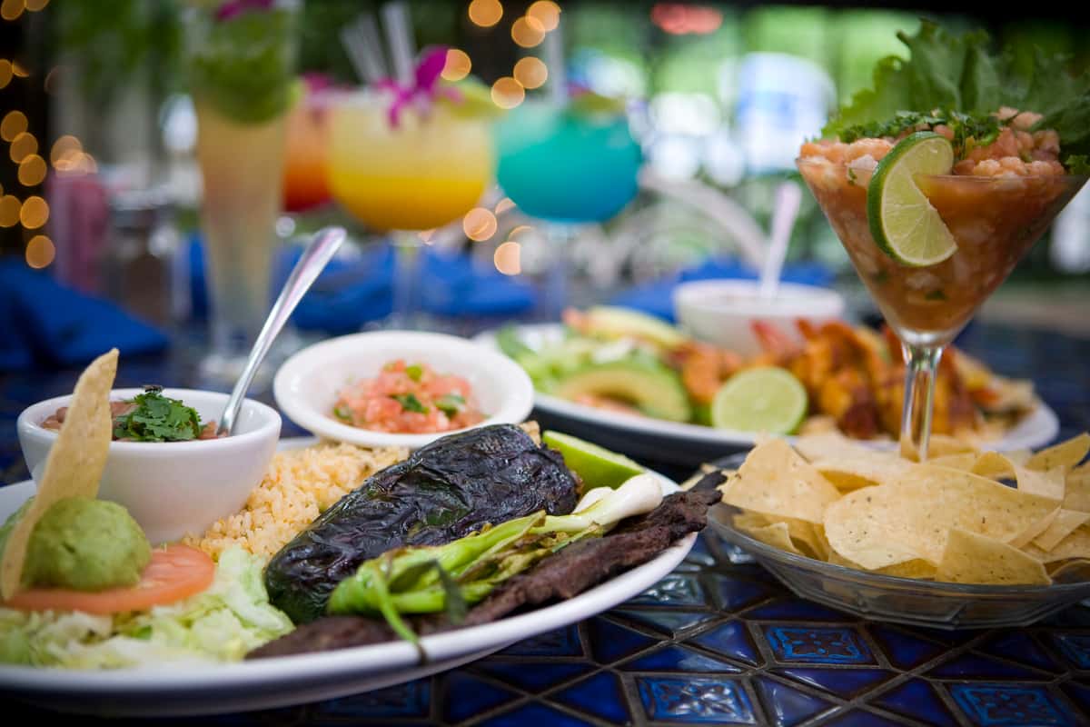 Mexican dinner spread with chips and salsa, grilled steak, stuffed chile, rice, and colorful margaritas.