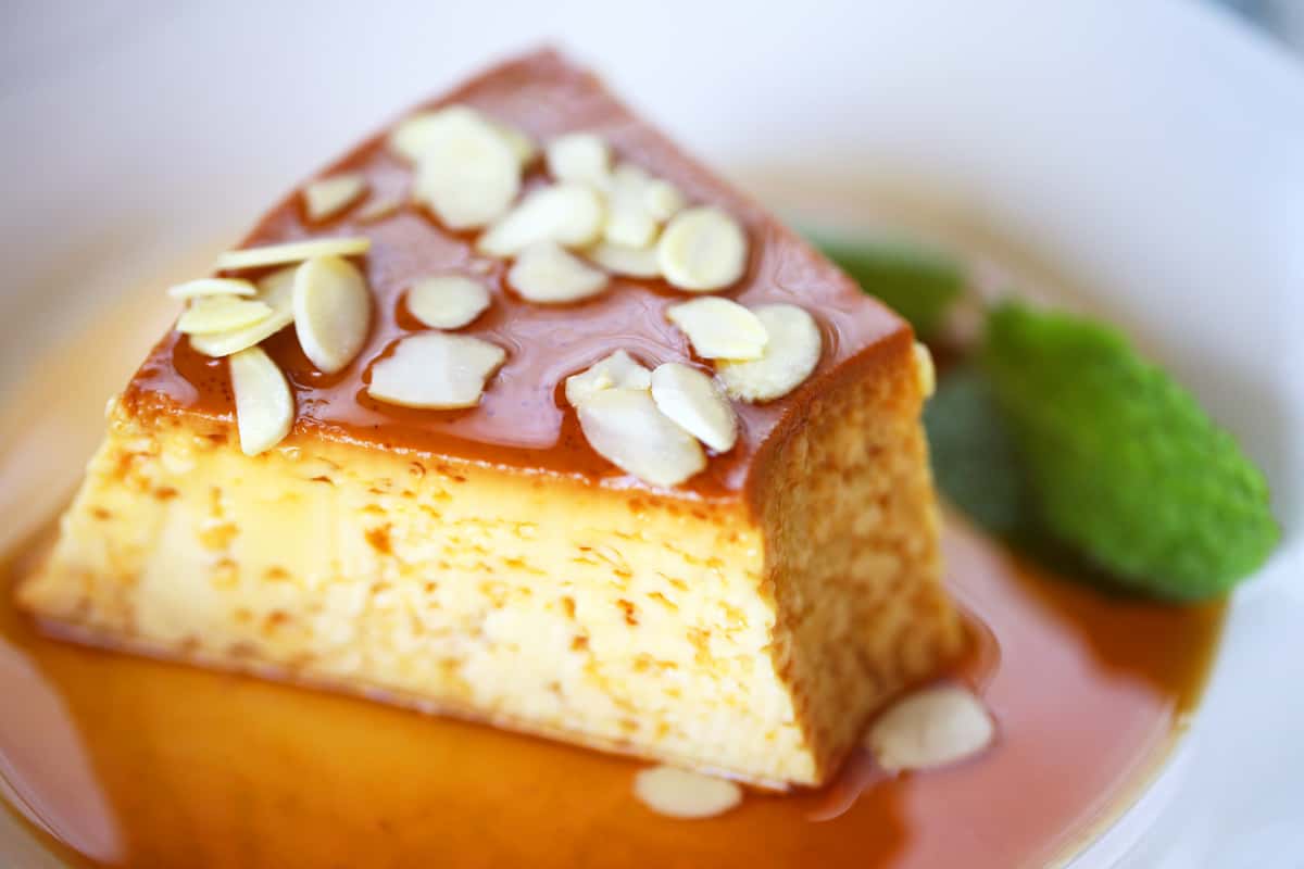 Slice of Mexican flan dessert topped with toasted almonds and caramel sauce, served with mint garnish.