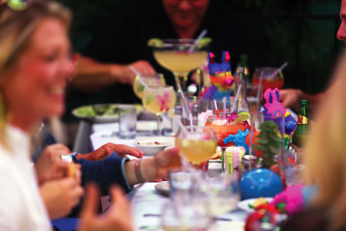 Guests enjoying colorful margaritas and cocktails at a lively Mexican restaurant table with festive drink garnishes.