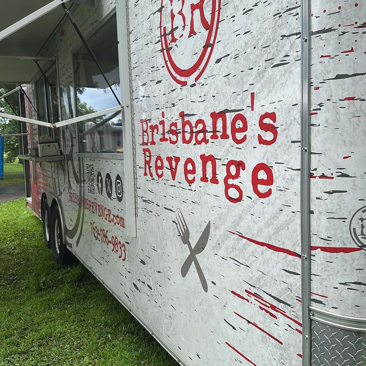 Side view of the Brisbane's Revenge food truck parked on grass with its service window open and bold red branding displayed.