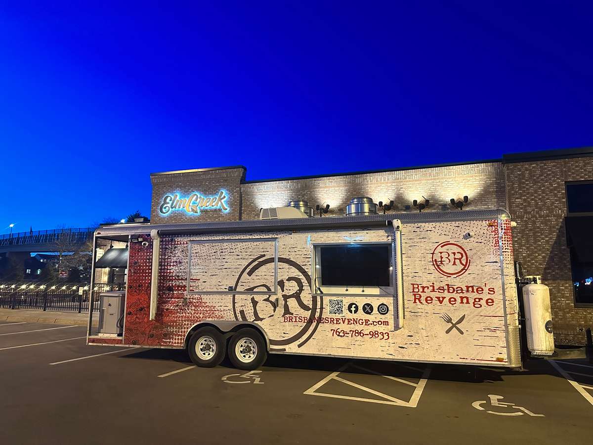 Brisbane's Revenge food truck parked outside Elm Creek restaurant under a deep blue evening sky, lights illuminating the scene.