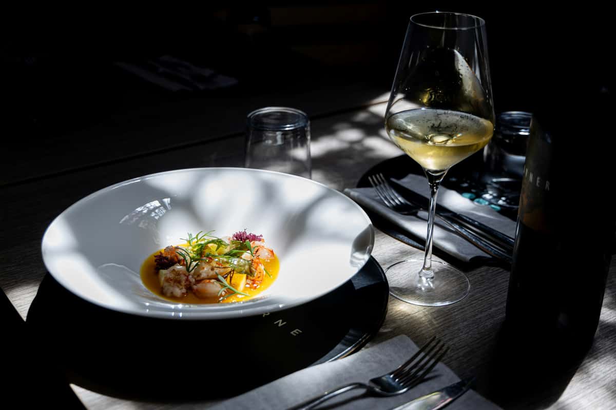 Gourmet seafood dish in saffron sauce garnished with herbs, served with chilled white wine in an upscale, moody dining setting.