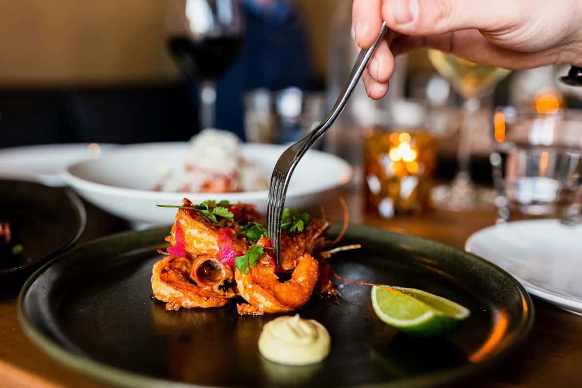 Crispy fried shrimp garnished with herbs and pickled onions, served with aioli and lime wedge in an elegant fine dining setting.
